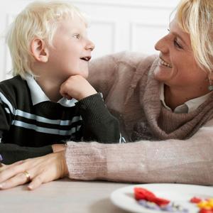 Barn og kvinde sidder ved bord, smiler til hinanden
