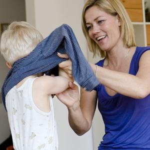 kvinde hjælper et barn med at tage trøje på