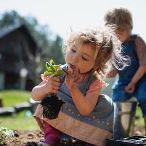Pige sidder på hug og kigger på plante. I baggrunden graver dreng i jorden.