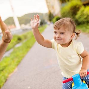 Barn på løbecykel giver high five til voksen