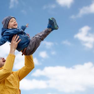 far svinger barn i luften, blå himmel