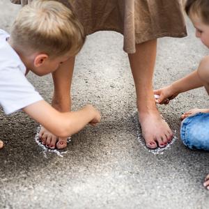 to drenge tegner med kridt rundt om en pædagogs fødder
