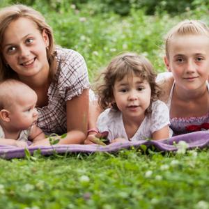 Fire børn i forskellige aldre ligger på tæppe i græsset