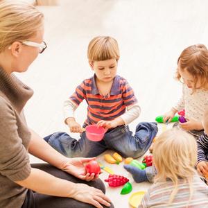 Kvinde sidder på gulvet sammen med en gruppe børn. De leger med frugt.