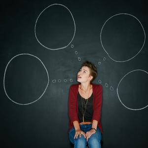 Foto af kvinde, der sidder med tomme tankebobler foran tavle