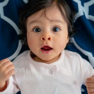 sorthåret baby med brune øjne kigger intenst og vågent, liggende på ryggen 