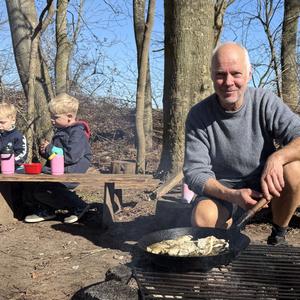 Pædagog Thomas Lyster tilbereder fisk over bål, mens et bar børn ser til