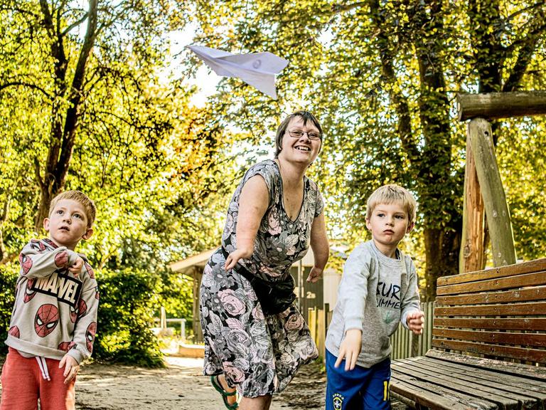 Pædagog Charlotte Andersen leger med papirsflyver med to børn