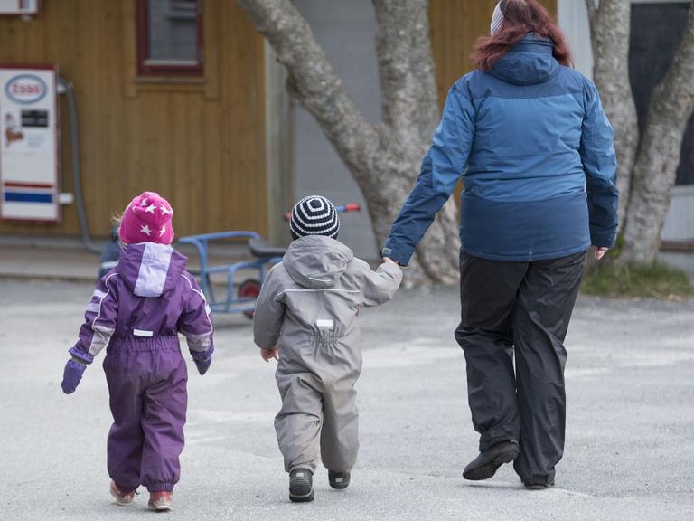 Pædagog i vintertøj på legeplads med to børn i flyverdragt