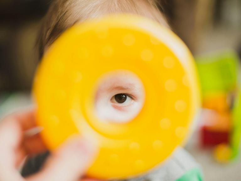 Lille barn kigger gennem gul plastikring, som pædagog holder.