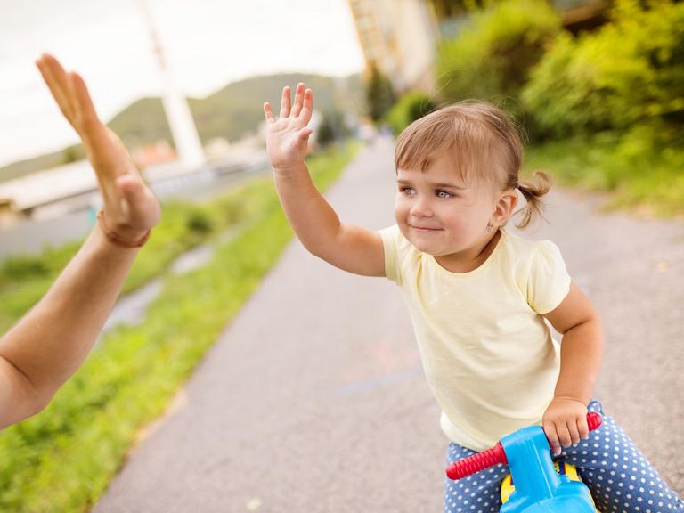 Barn på løbecykel giver high five til voksen