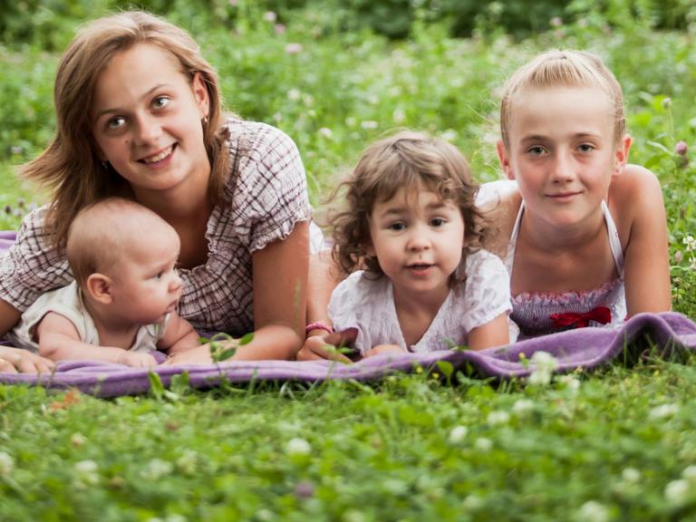 Fire børn i forskellige aldre ligger på tæppe i græsset