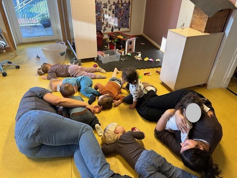 Foto af børn og pædagoger, der leger på gulv