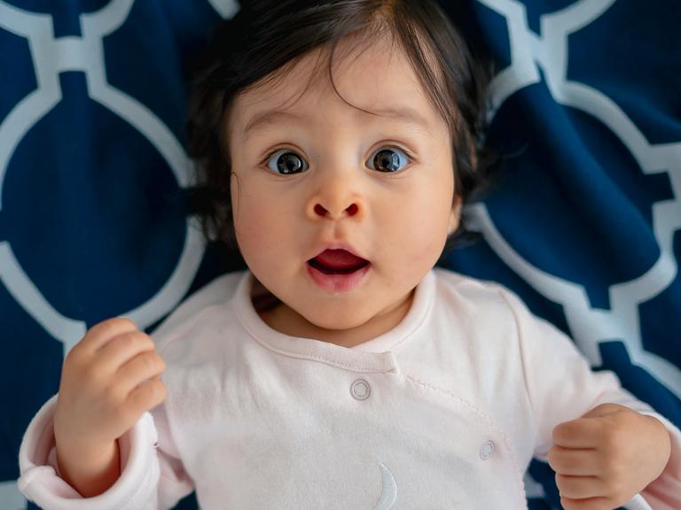 sorthåret baby med brune øjne kigger intenst og vågent, liggende på ryggen 