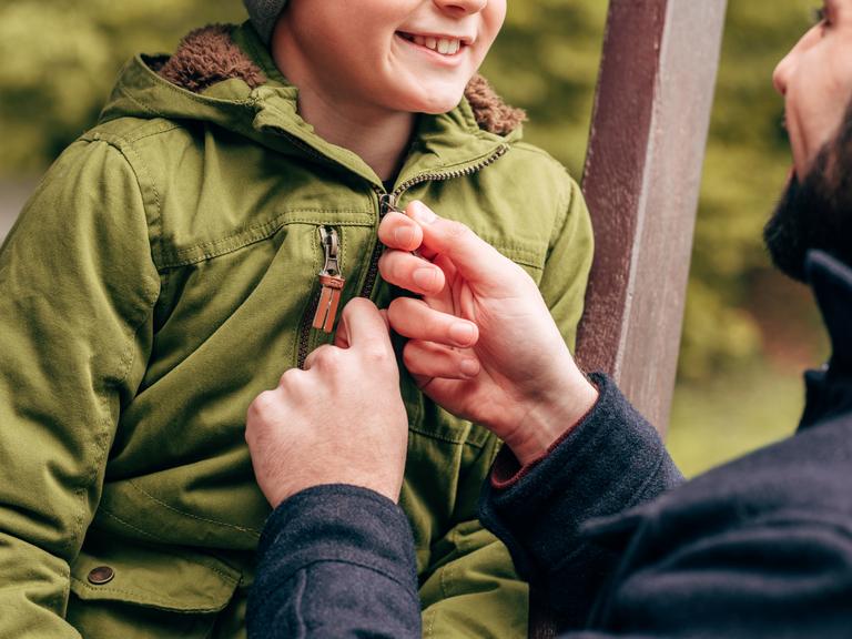 mandlig pædagog lyner skoledrengs jakke, viser omsorg, smiler