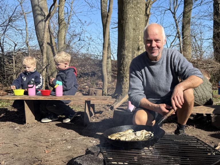 Pædagog Thomas Lyster tilbereder fisk over bål, mens et bar børn ser til