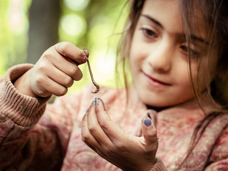 pige i naturen, kigger på og holder regnorm i den ene ende