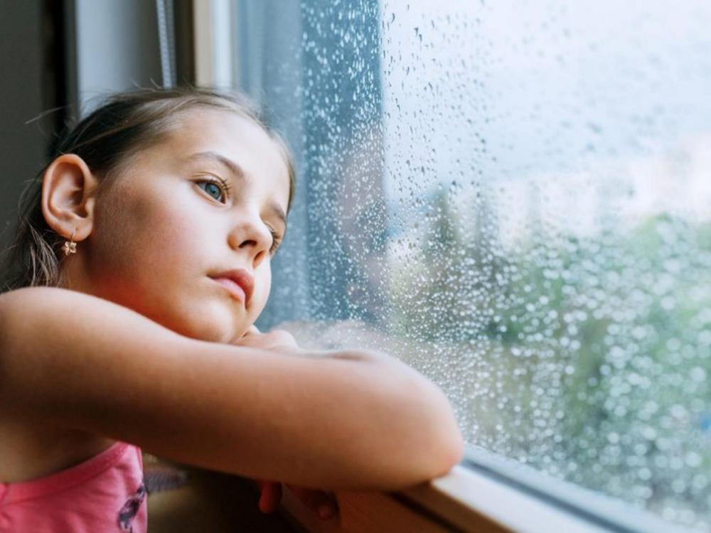 billede af pige, der sidder ved regnvådt vindue