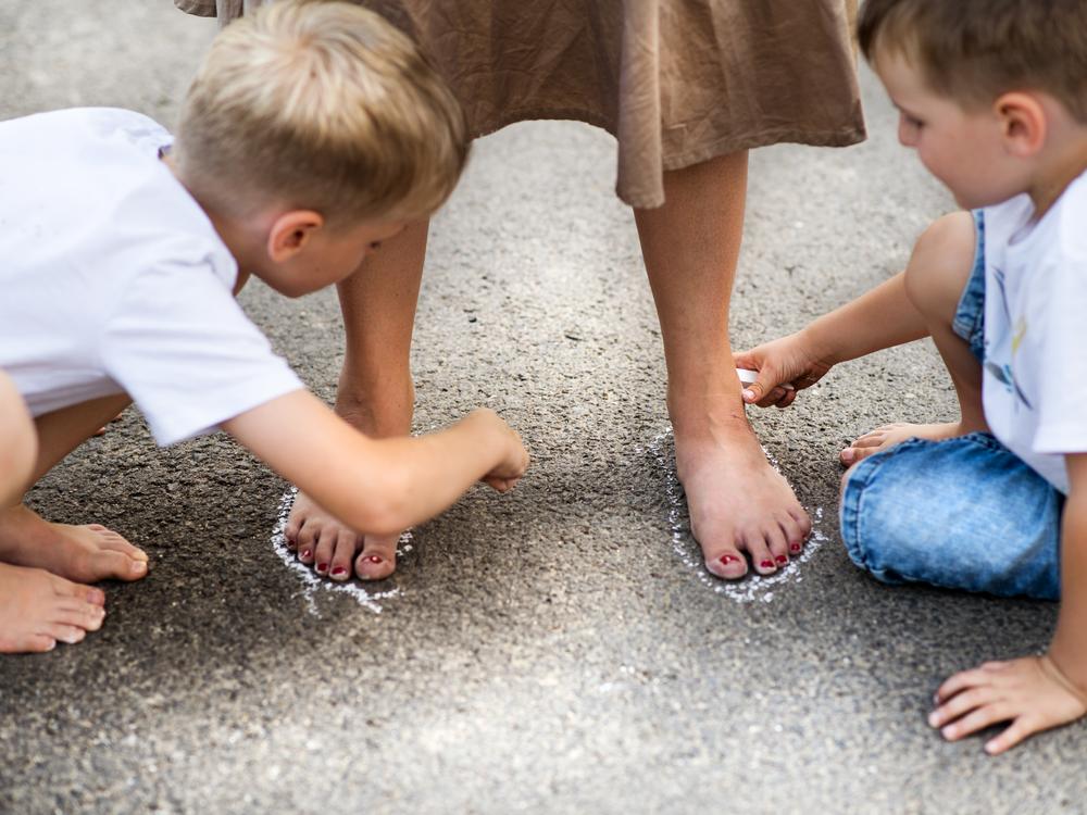 to drenge tegner med kridt rundt om en pædagogs fødder