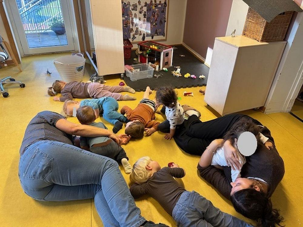 Foto af børn og pædagoger, der leger på gulv