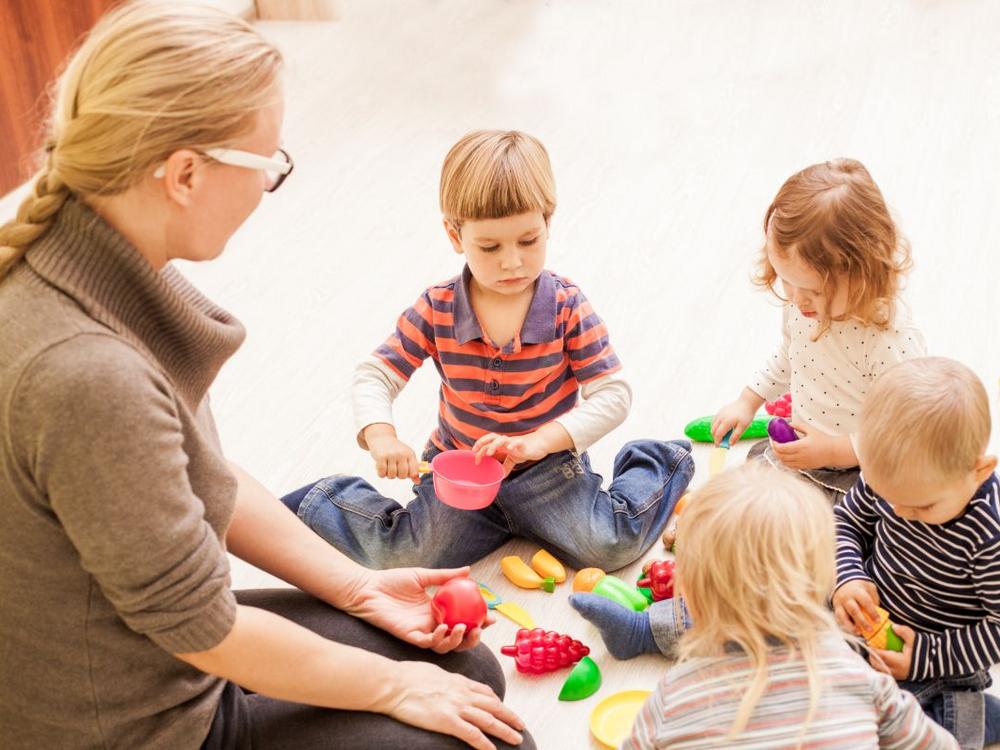 Kvinde sidder på gulvet sammen med en gruppe børn. De leger med frugt.