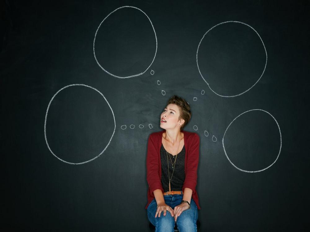 Foto af kvinde, der sidder med tomme tankebobler foran tavle