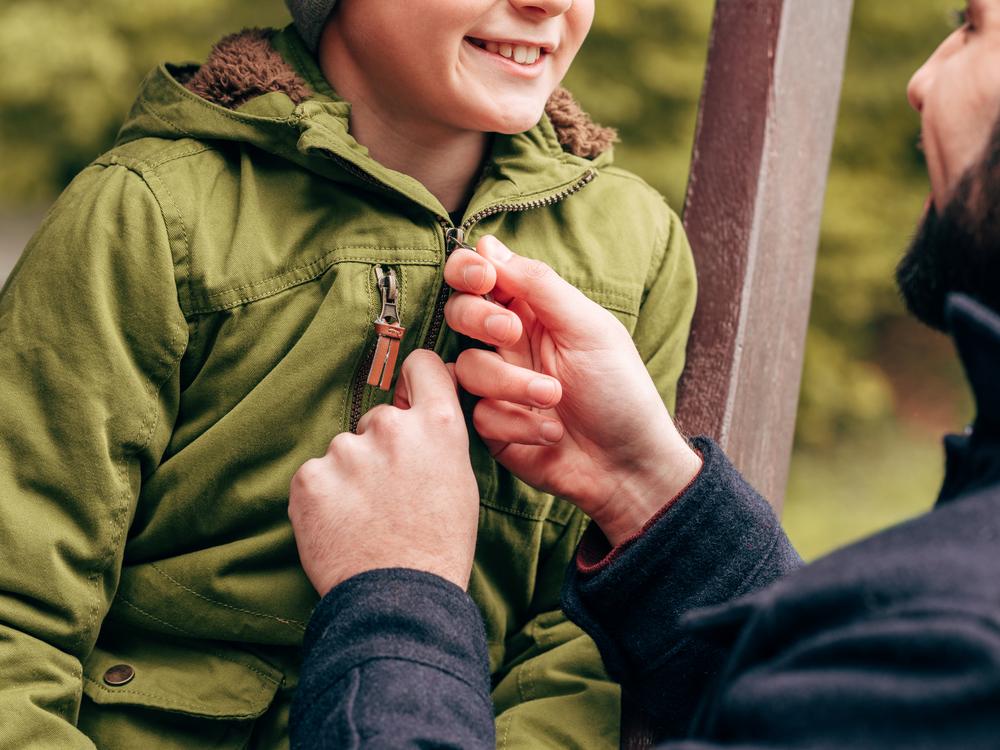 mandlig pædagog lyner skoledrengs jakke, viser omsorg, smiler